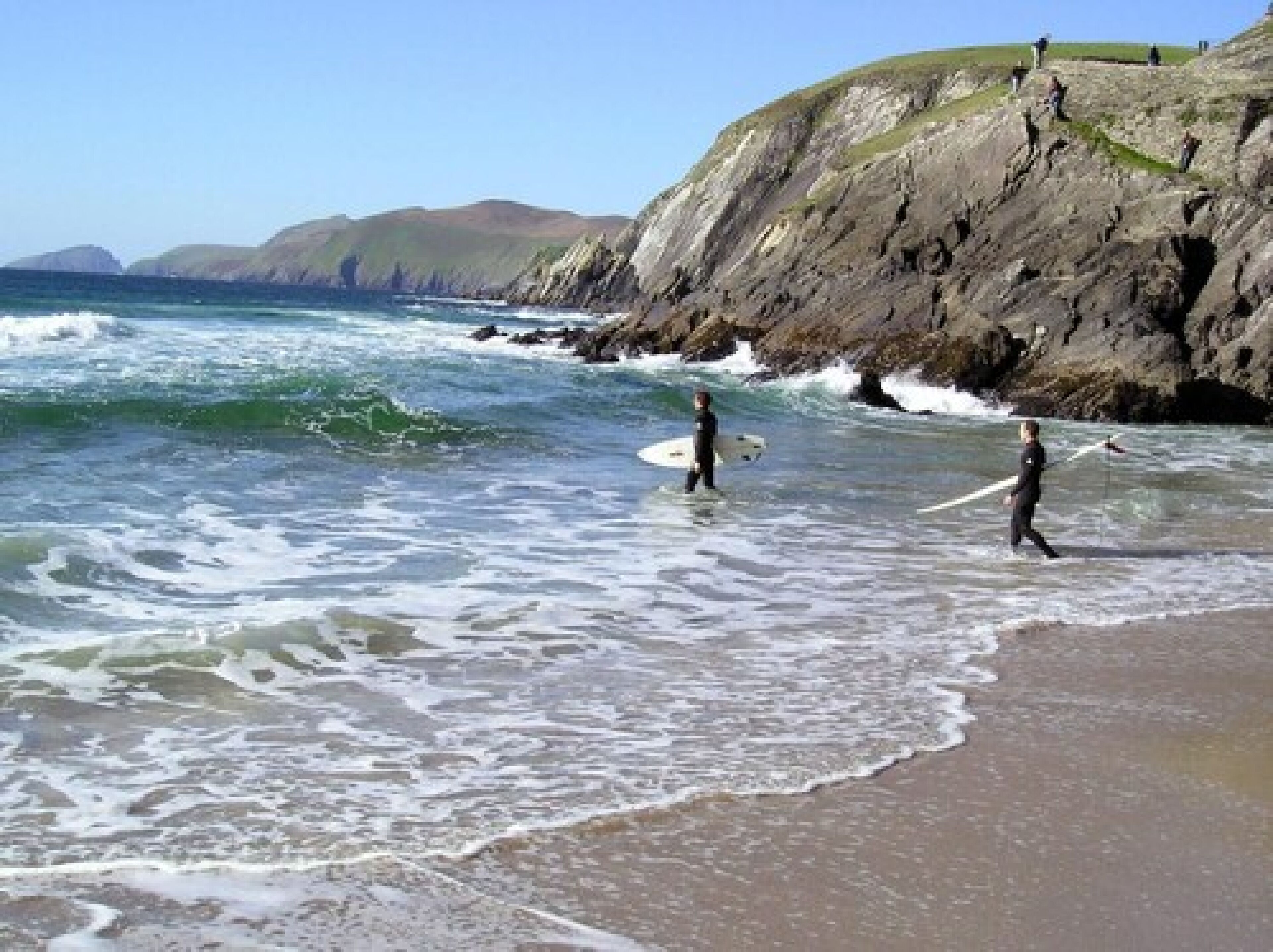 Una playa con olas y acantilados al fondo.