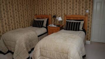 A room with two single beds, wooden headboards, a nightstand with a lamp, and patterned wallpaper.