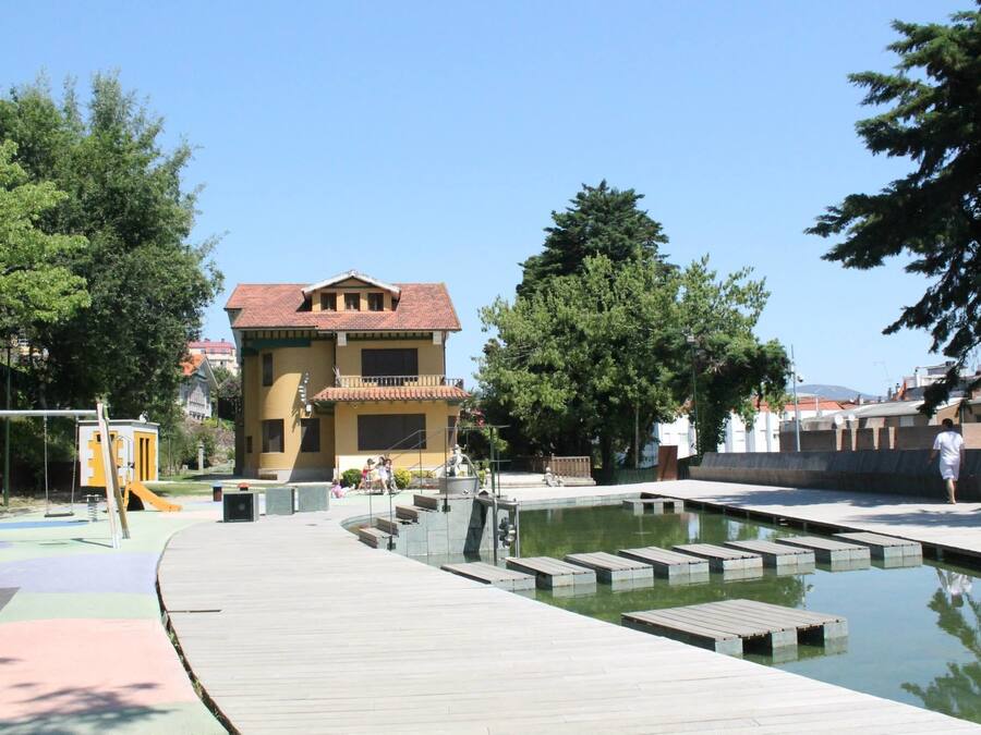 A public park with a swimming pool, playground, and a building with a red-tiled roof.