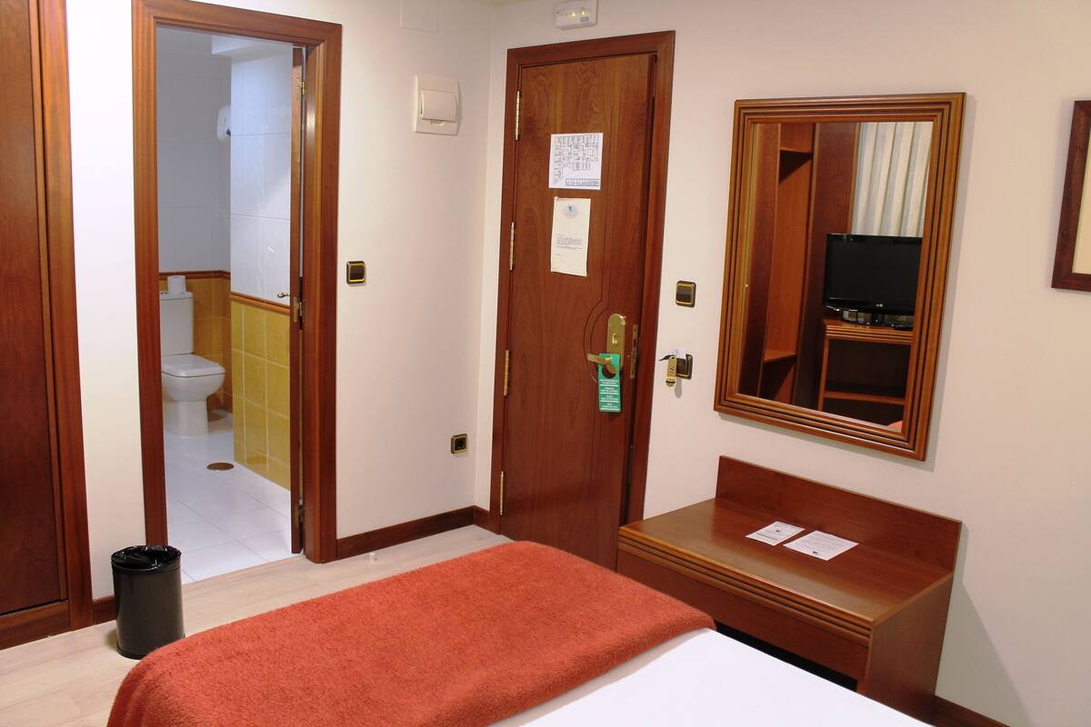 Une chambre d’hôtel avec un lit, un banc en bois, une télévision et un miroir au mur.