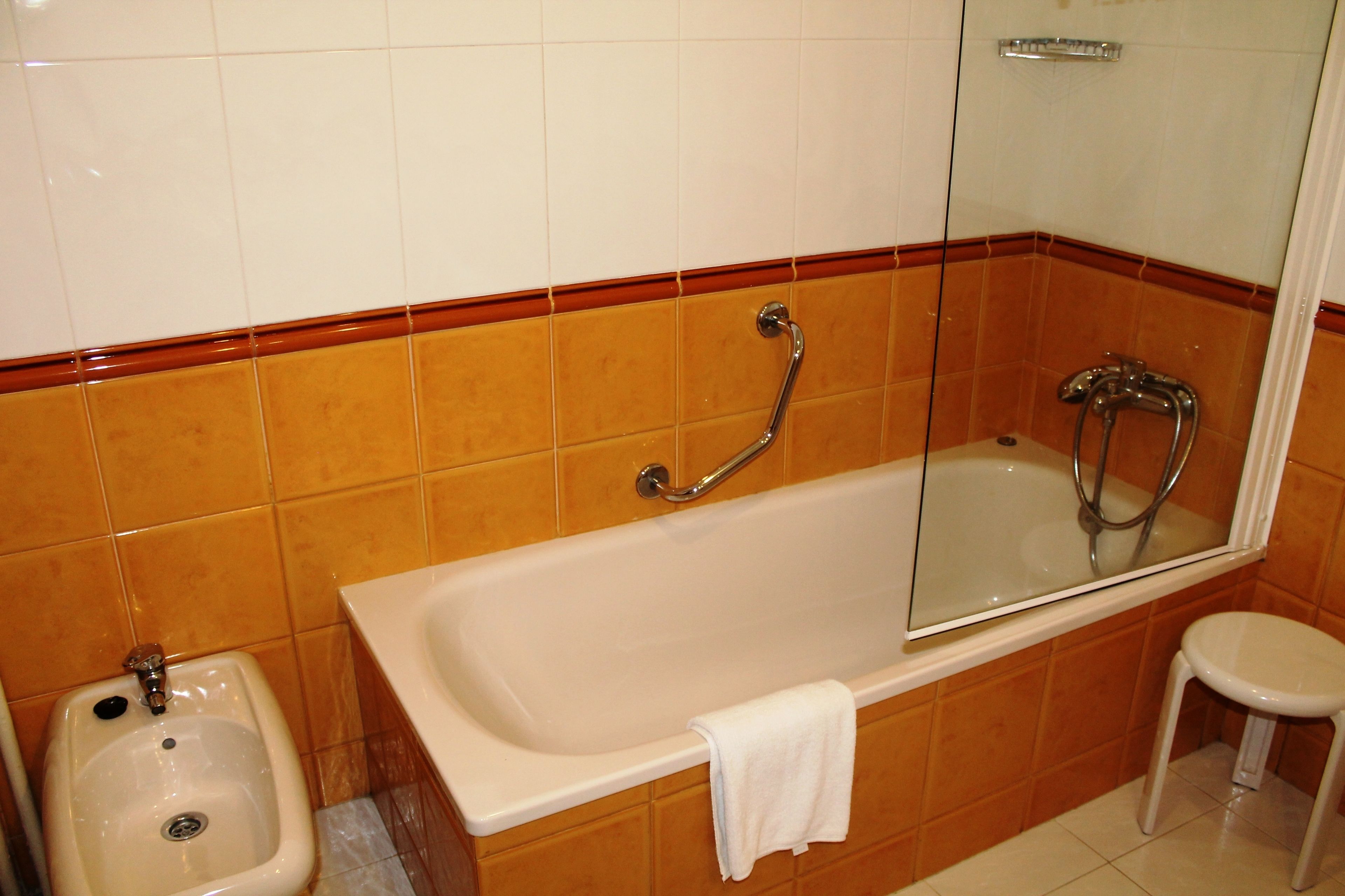 A bathroom with a bathtub, a shower, a bidet, and a small stool.