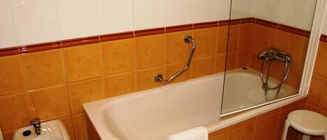 A bathroom with a bathtub, a shower, a bidet, and a small stool.