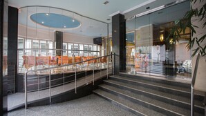 Un interior moderno con techo curvo, una escalera con barandilla de metal y una zona de estar con sillas anaranjadas.