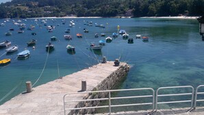 Un puerto con numerosas embarcaciones ancladas en aguas claras, un muelle de piedra y una costa distante con edificios.