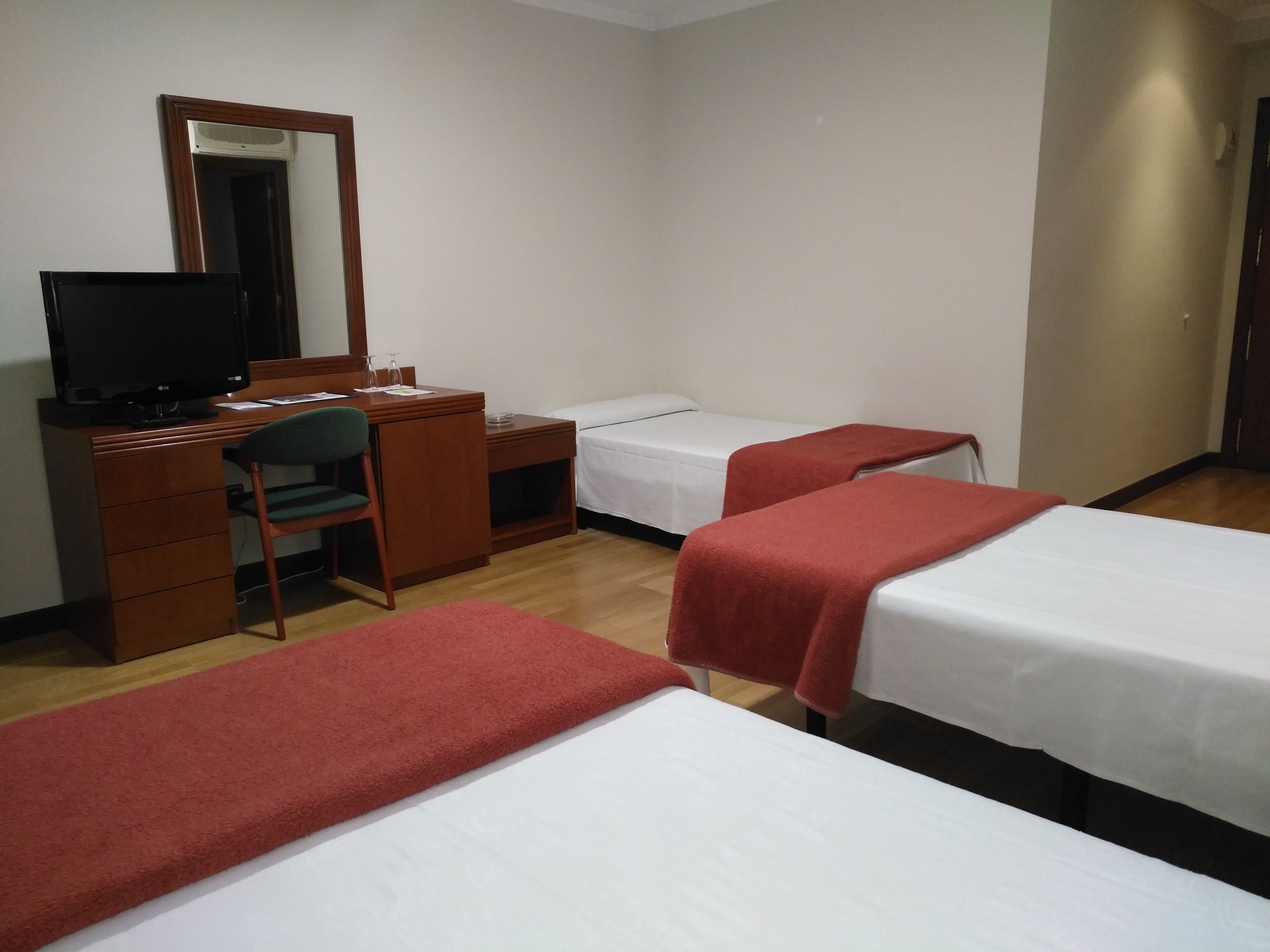 A hotel room with two single beds, a desk with a chair, a television, and a mirror.