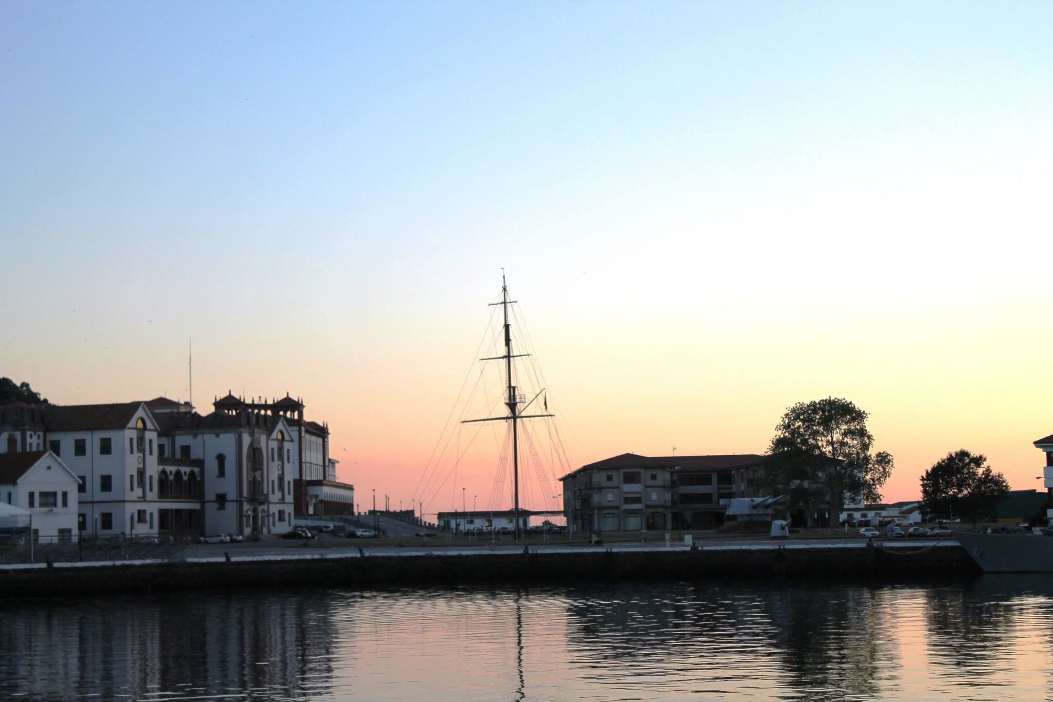 A waterfront building with a prominent tall structure in the center, likely a ship or tower, and a calm water body reflecting the building.