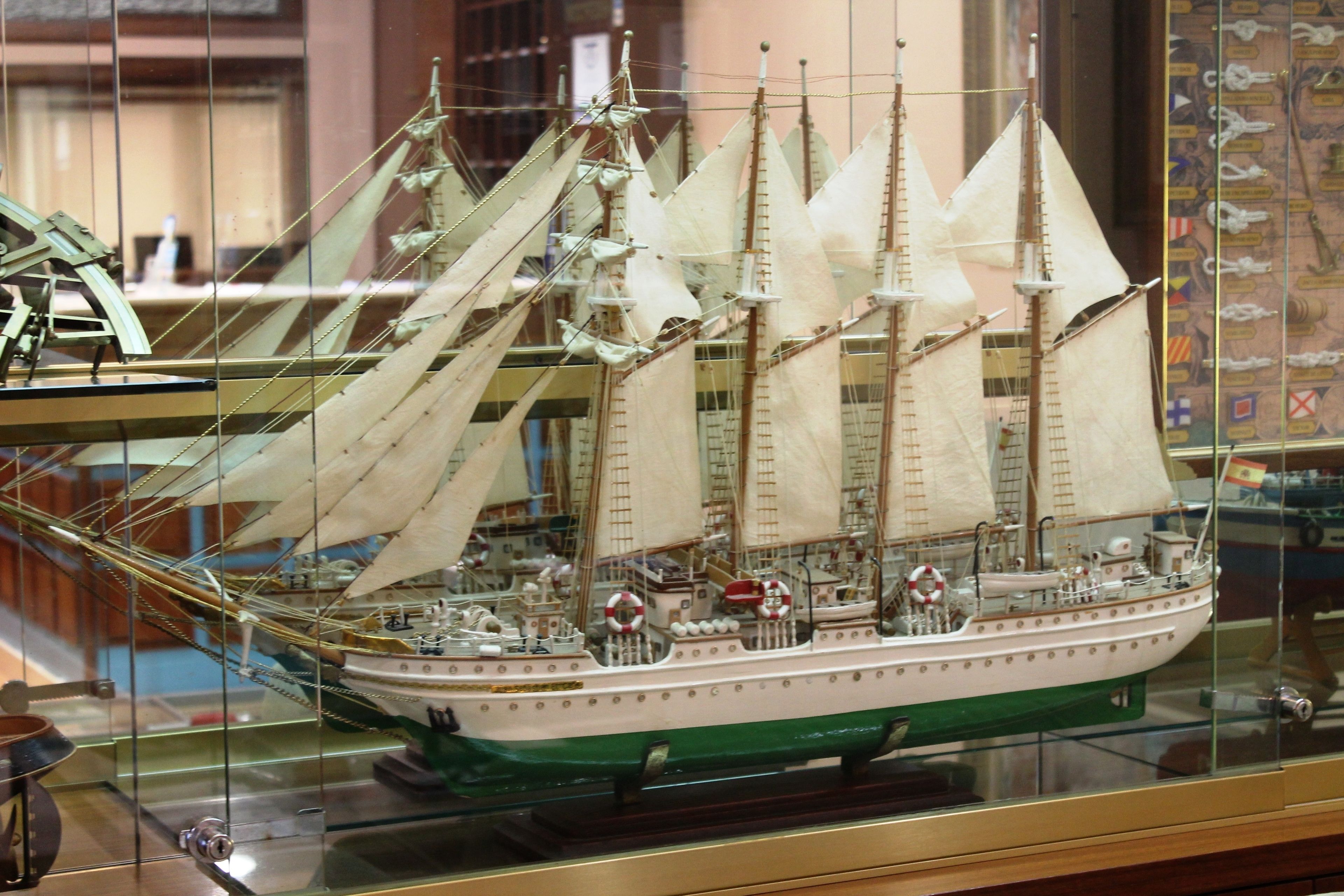 A model ship with multiple sails and a detailed deck, displayed in a glass case.