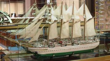 A model ship with multiple sails and a detailed deck, displayed in a glass case.