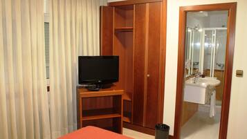A hotel room with a bed, a television, a wardrobe, a bathroom with a sink and mirror, and a trash bin.