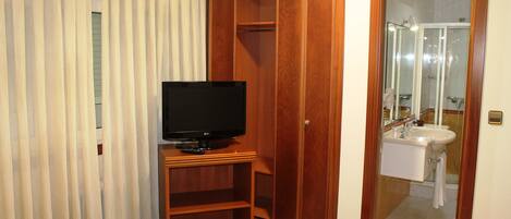 A hotel room with a bed, a television, a wardrobe, a bathroom with a sink and mirror, and a trash bin.