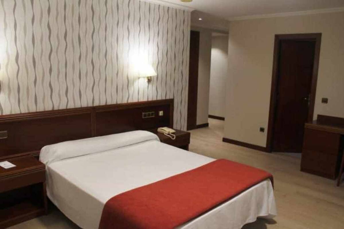 Une chambre d’hôtel avec un lit, une table de chevet, une lampe et une porte.
