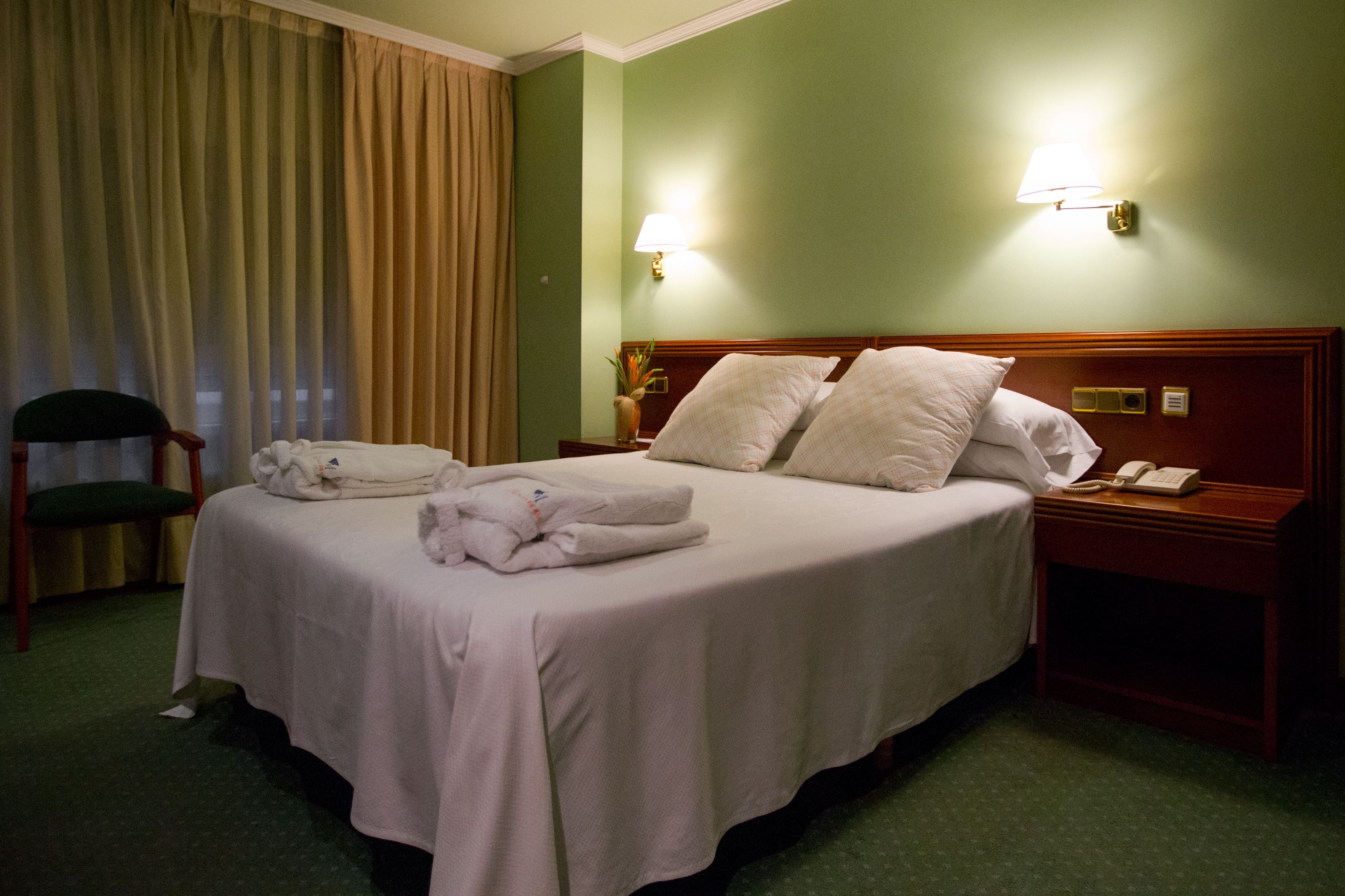 Een hotelkamer met een opgemaakt bed, een bedlampje, een telefoon en een stoel.