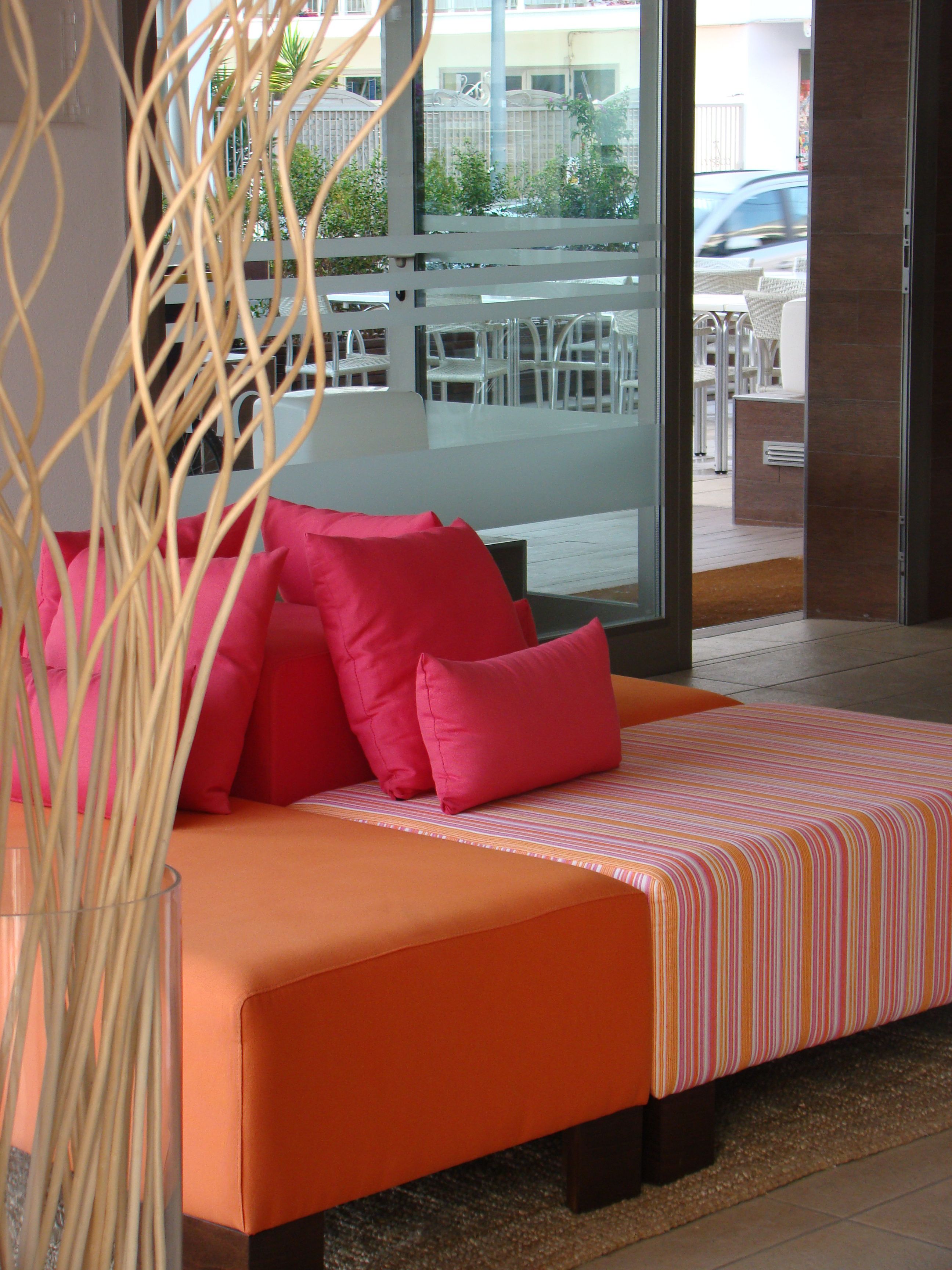 Une chambre d’hôtel moderne avec un grand lit, une literie orange et une vue sur la rue, visible à travers une porte vitrée.