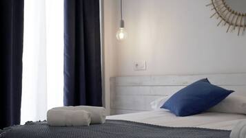 Una cama bien hecha con una almohada azul, una almohada blanca y una toalla blanca enrollada.