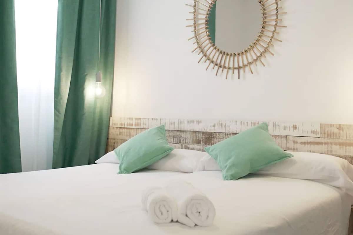 Una cama bien tendida con sábanas blancas y almohadas verdes, una decoración circular de madera en la pared y un cabecero de madera.