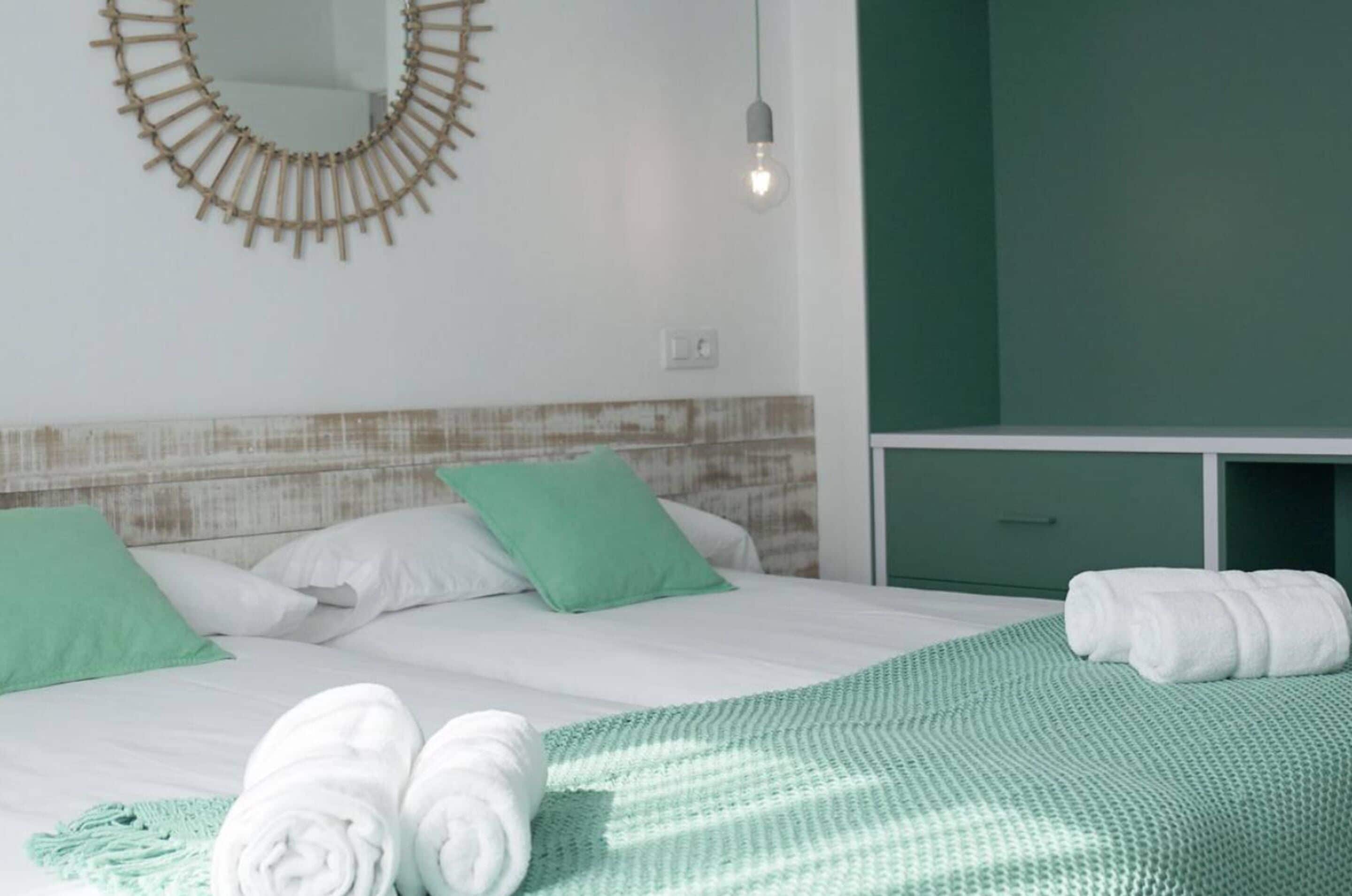 A hotel room with a bed, green pillows, a green blanket, and a towel on the bed.