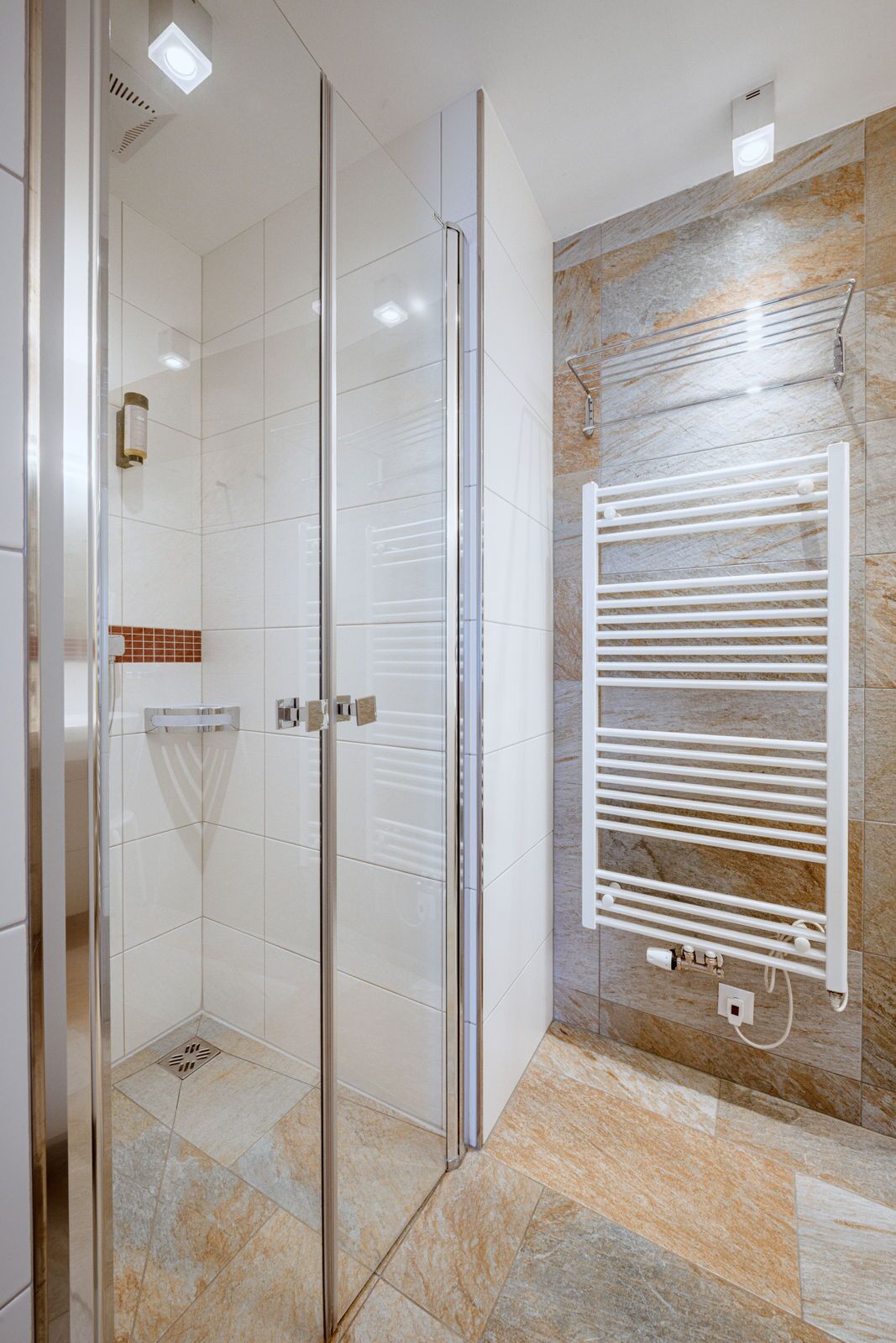 A modern bathroom with a glass shower enclosure, a white towel rack, and a marble-tiled wall.