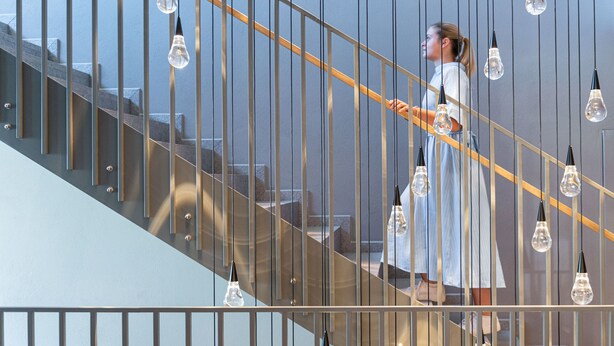Un escalier avec une rampe en métal et des luminaires suspendus.