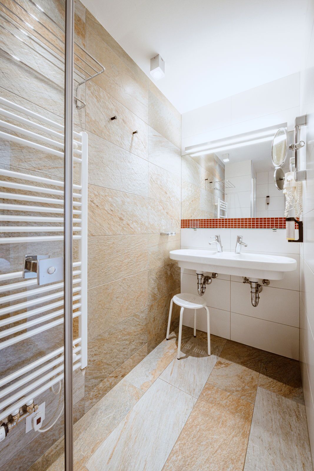 Un baño moderno con cabina de ducha de vidrio, un lavabo blanco y un revoque de azulejos rojos.