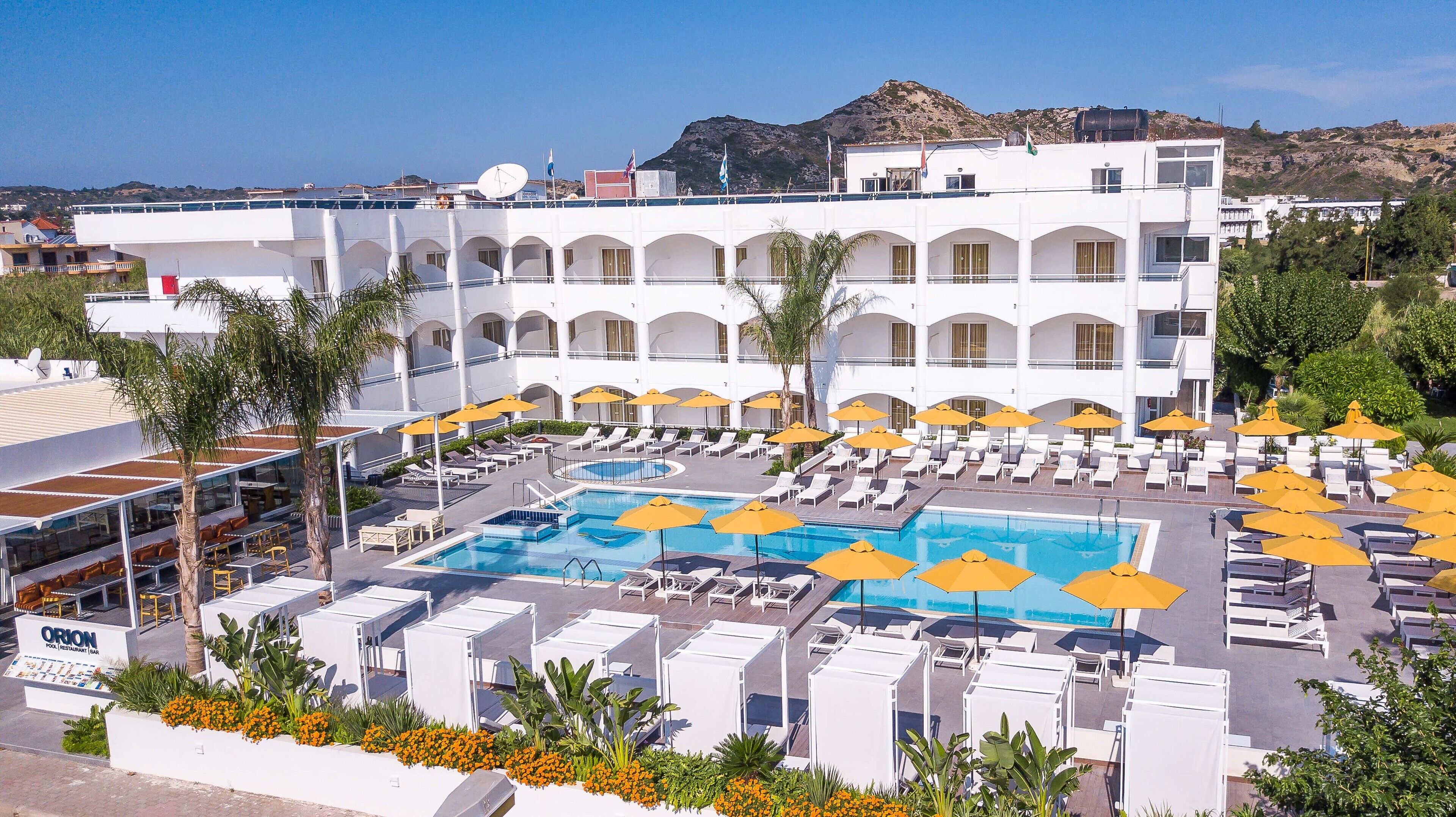 Un hôtel doté d’une piscine entourée de transats et de parasols, d’un restaurant et offrant une vue sur la mer.