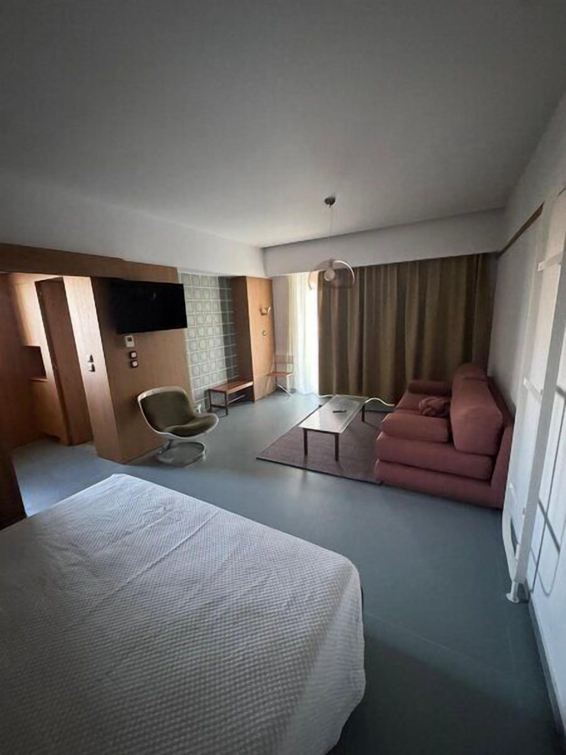 Habitación de hotel con cama, sofá, mesita, sillón y televisor.