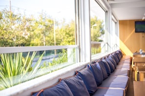 A row of blue cushioned seating along a window with a view of greenery outside. - Orion Hotel Faliraki (Rhodes)