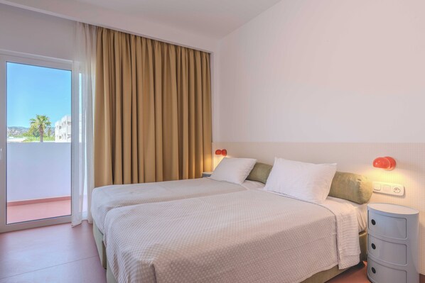 A hotel room with a large bed, two bedside tables, a nightstand, and a view of the outside.