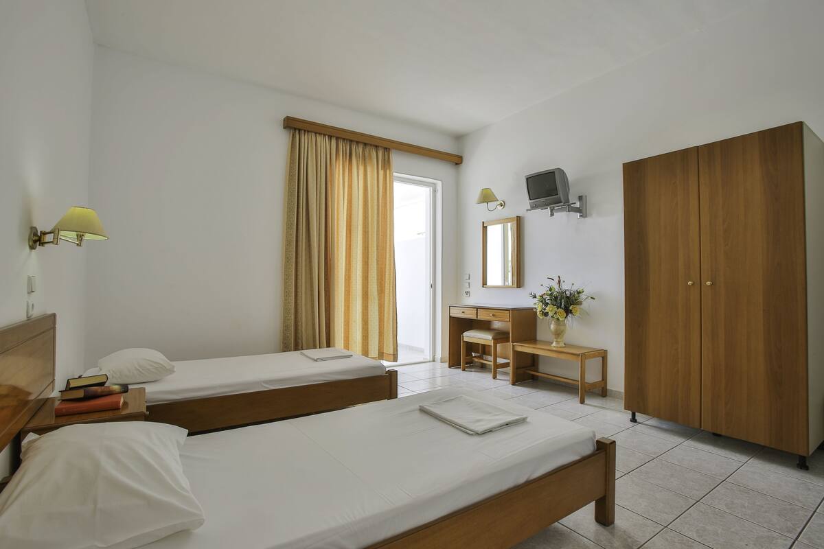 A hotel room with two single beds, a desk, a chair, a wardrobe, and a television.