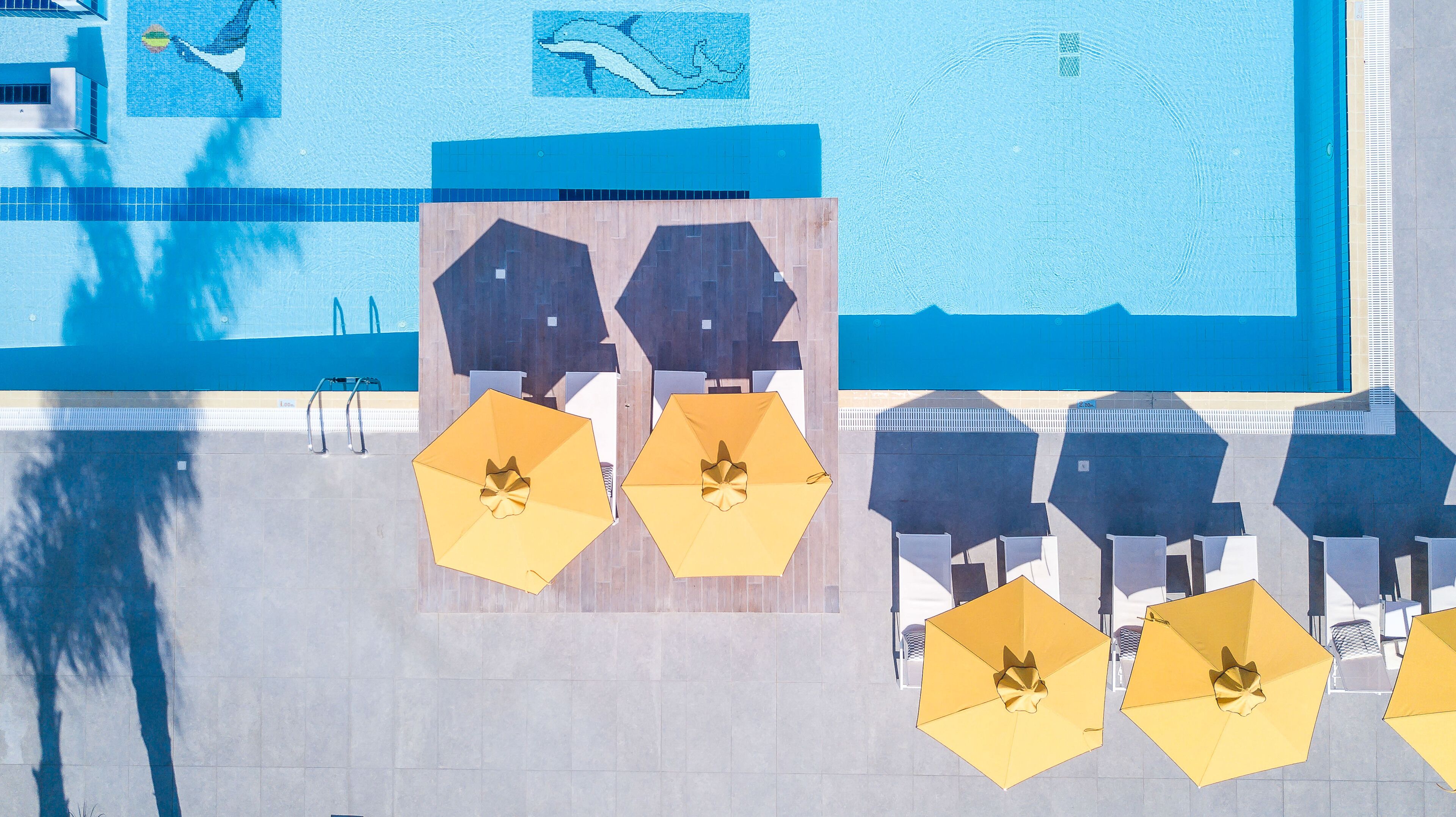 A rooftop pool area with multiple yellow umbrellas and lounge chairs, surrounded by a tiled deck.