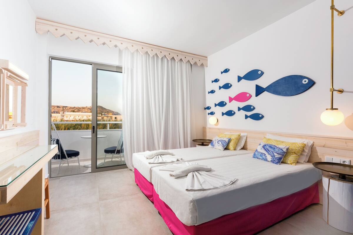 A hotel room with a bed, a desk, a chair, a balcony with a view, and a wall with fish decorations.