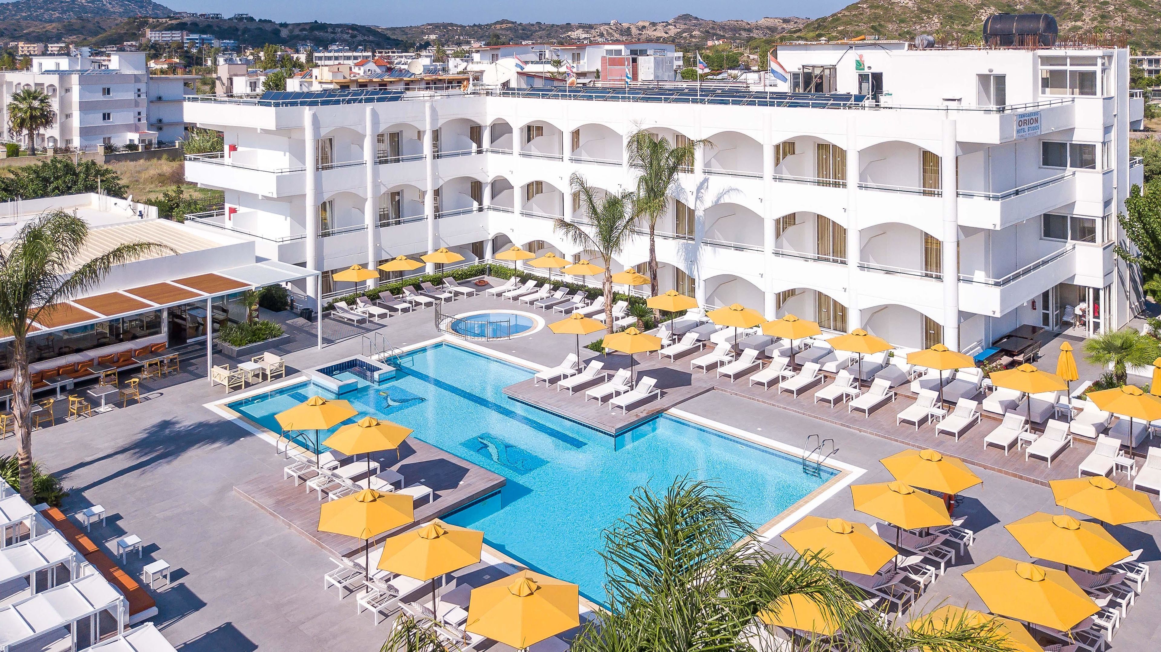 Un hotel con un amplio espacio de piscina, varios niveles de balcones y vistas del paisaje circundante.