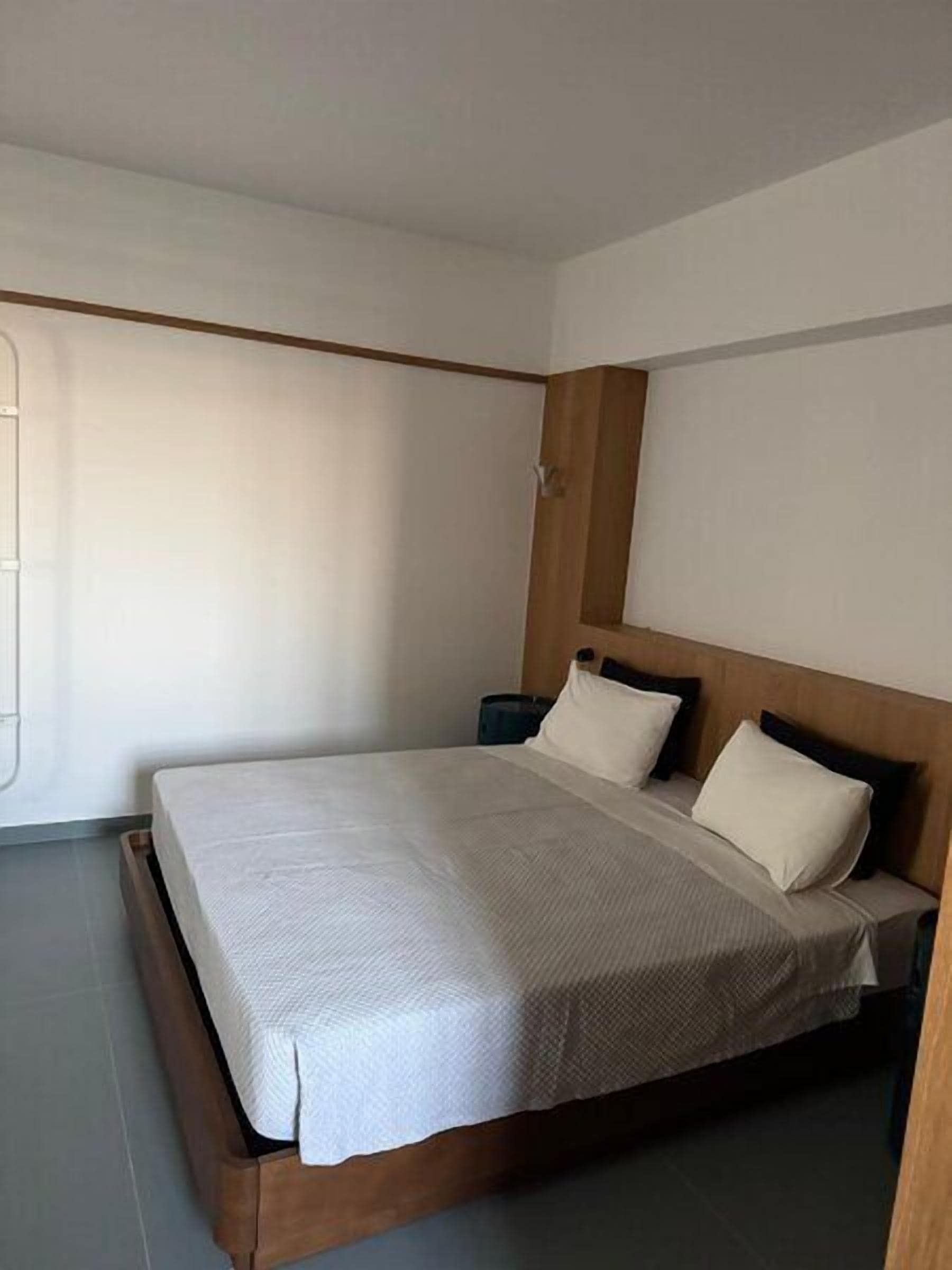 A single bed with a wooden headboard, a bedside table, and a window with blinds.