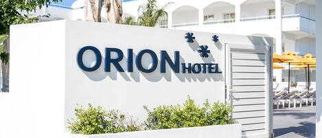 Señal de hotel con el nombre "ORION HOTEL" y una palmera en primer plano.