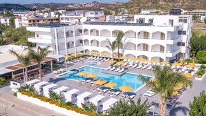Ett hotell med en stor pool omgiven av solstolar och parasoller, flera balkonger och utsikt över det omgivande landskapet.