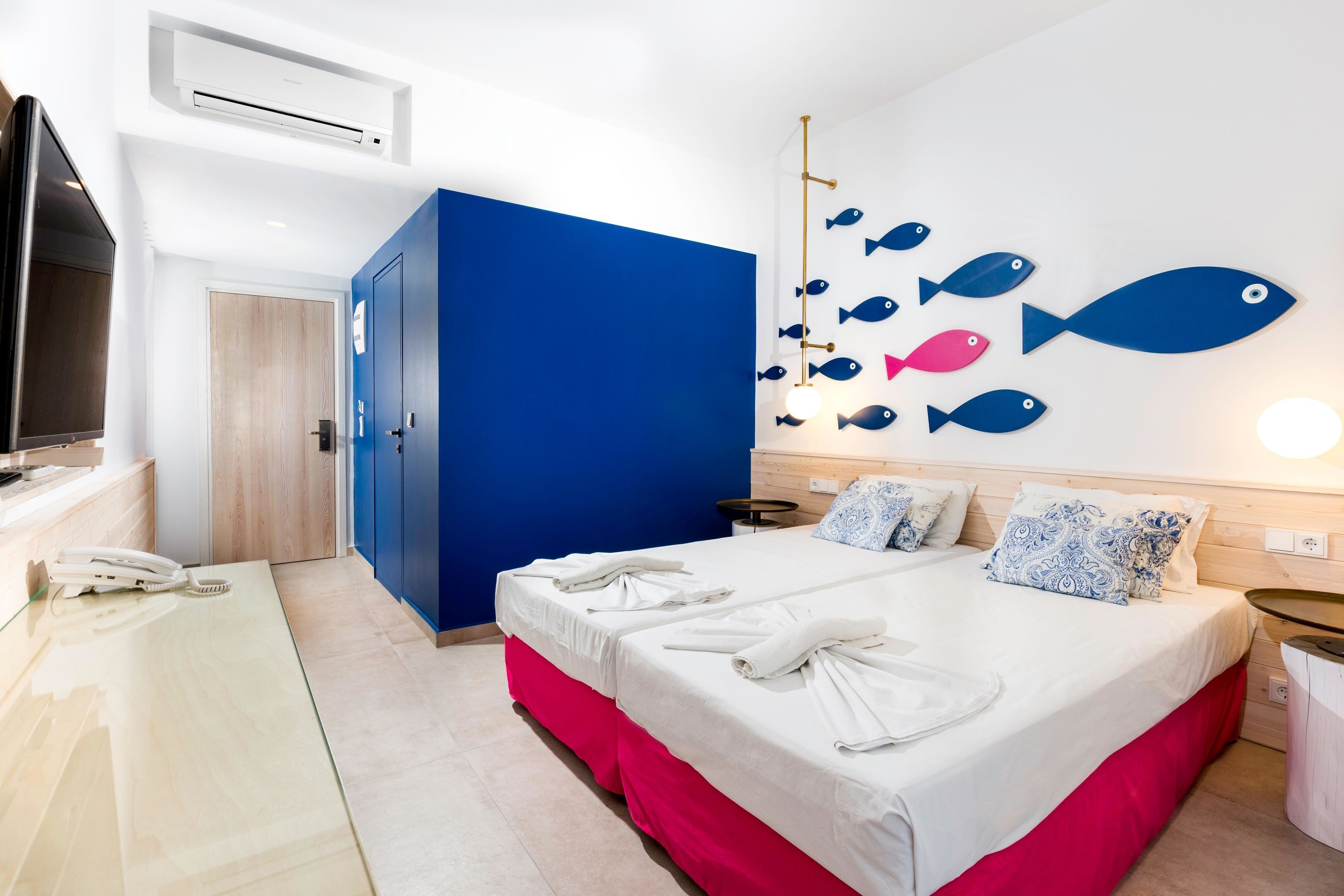 A hotel room with a bed, a desk, a chair, a phone, and a wall with fish decorations.