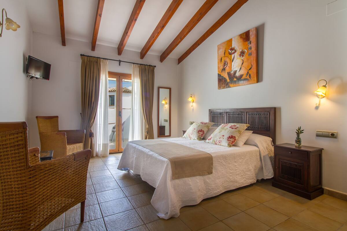 Ein Schlafzimmer mit einem Bett, einem Sessel, einem Nachttisch, einem Fernseher und einem Bild an der Wand.