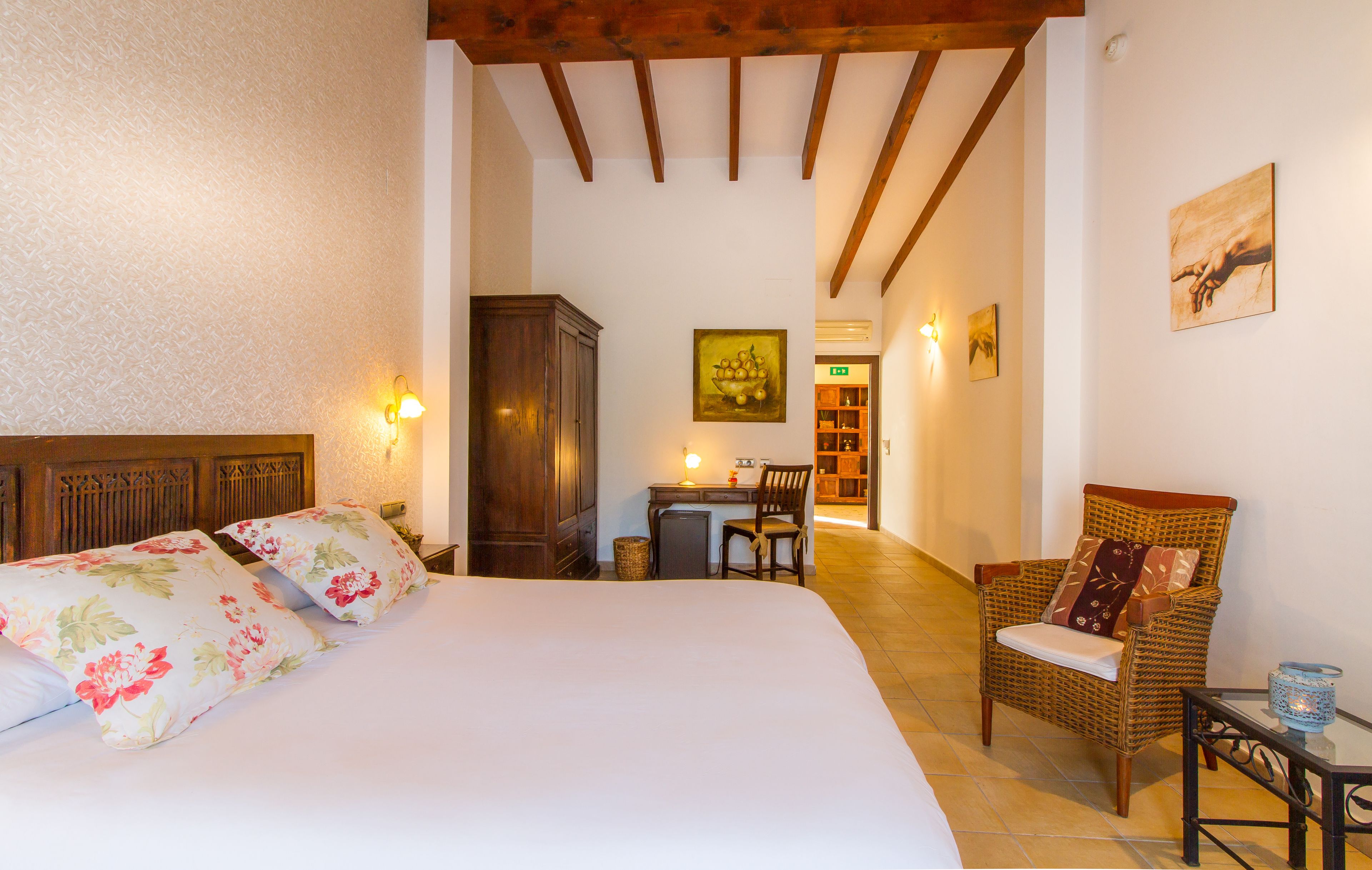 A bedroom with a large bed, a desk, a chair, and a small table with a lamp.