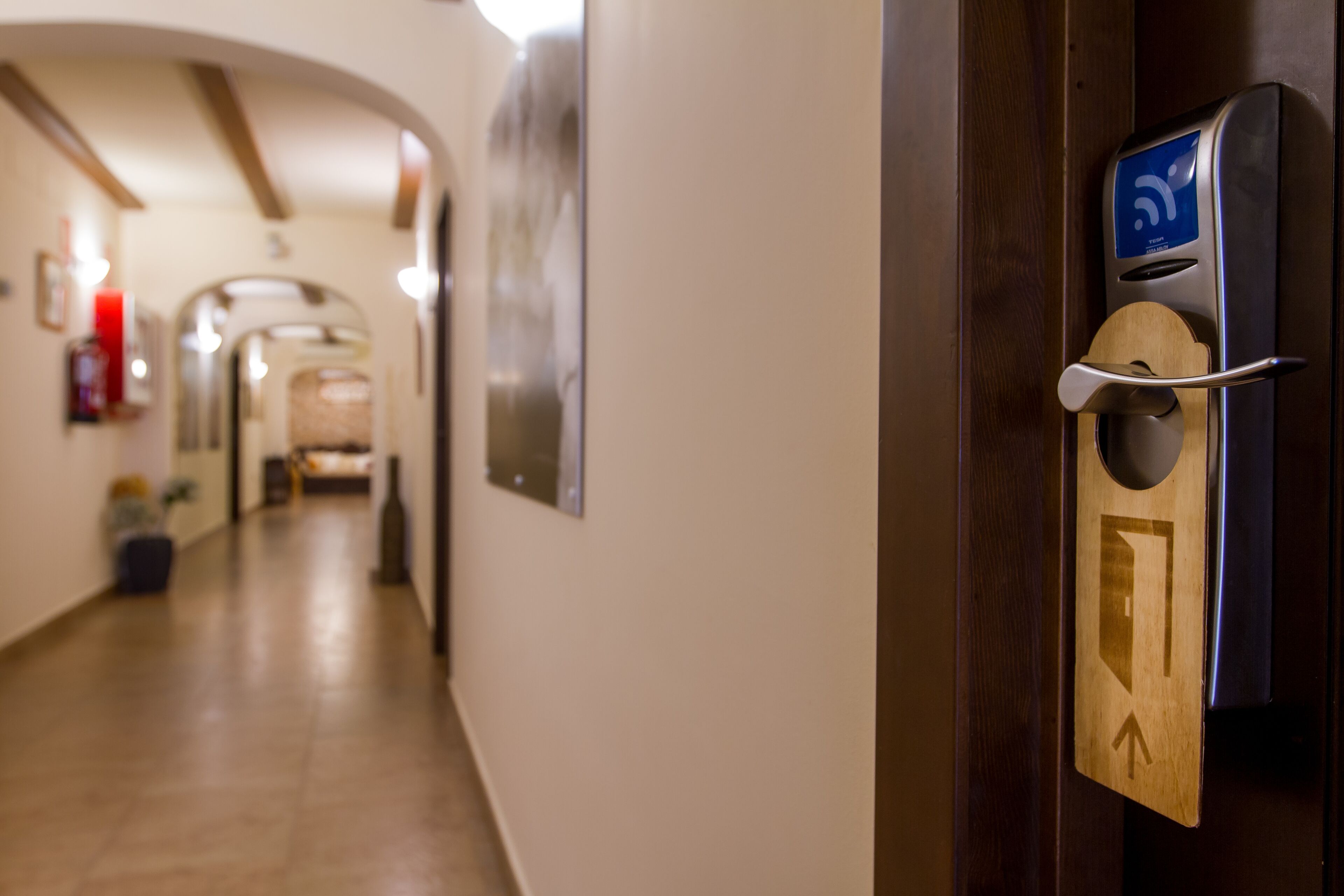 A hallway with a wooden door featuring a keycard reader and a directional arrow sign.