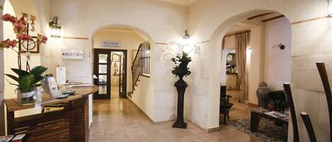 A reception area with a reception desk, a sign for 'MENADOR ALMA SERRA', and a staircase leading to another room.