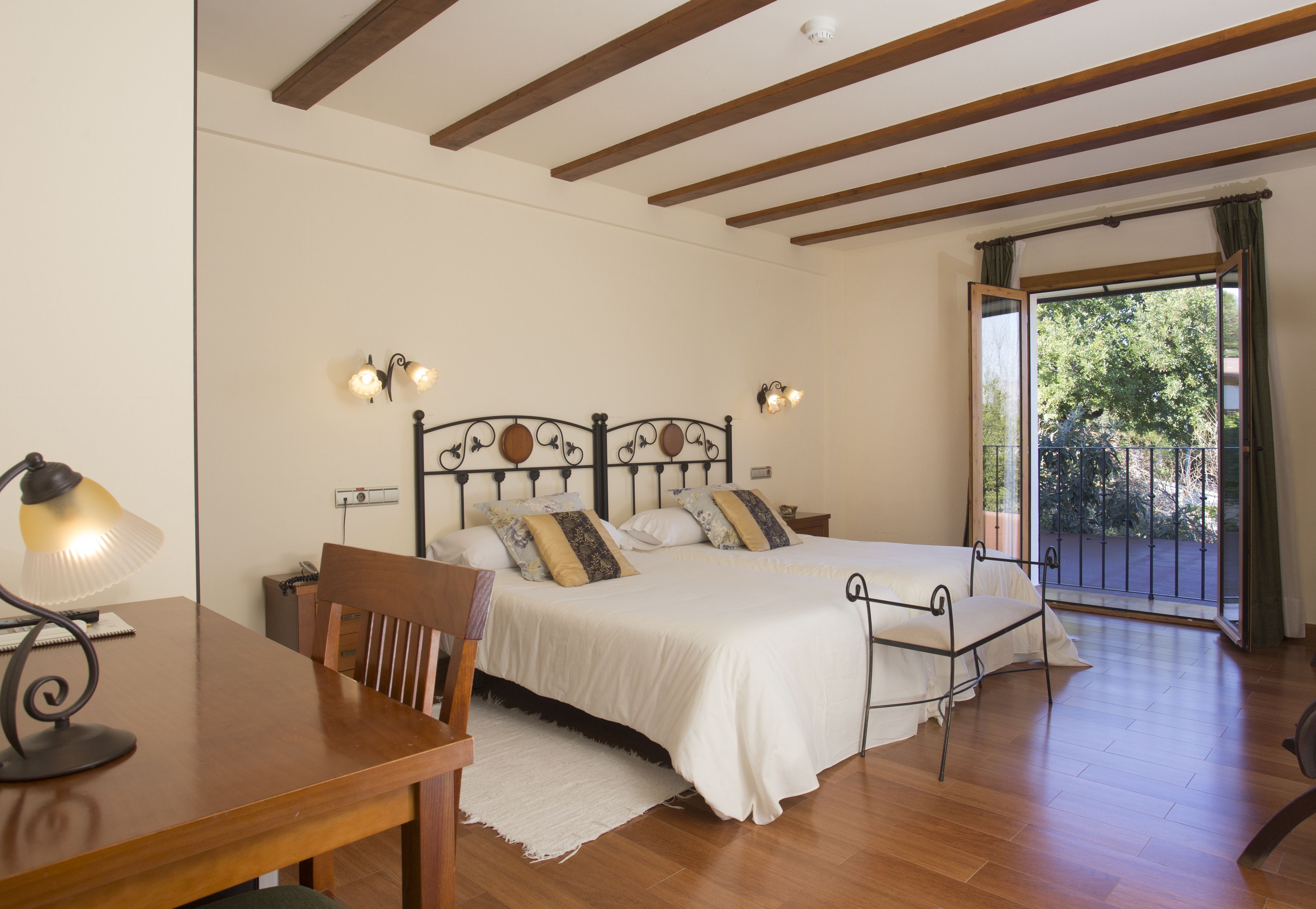 A bedroom with a bed, a desk, and a chair. There is a window with a view of trees.