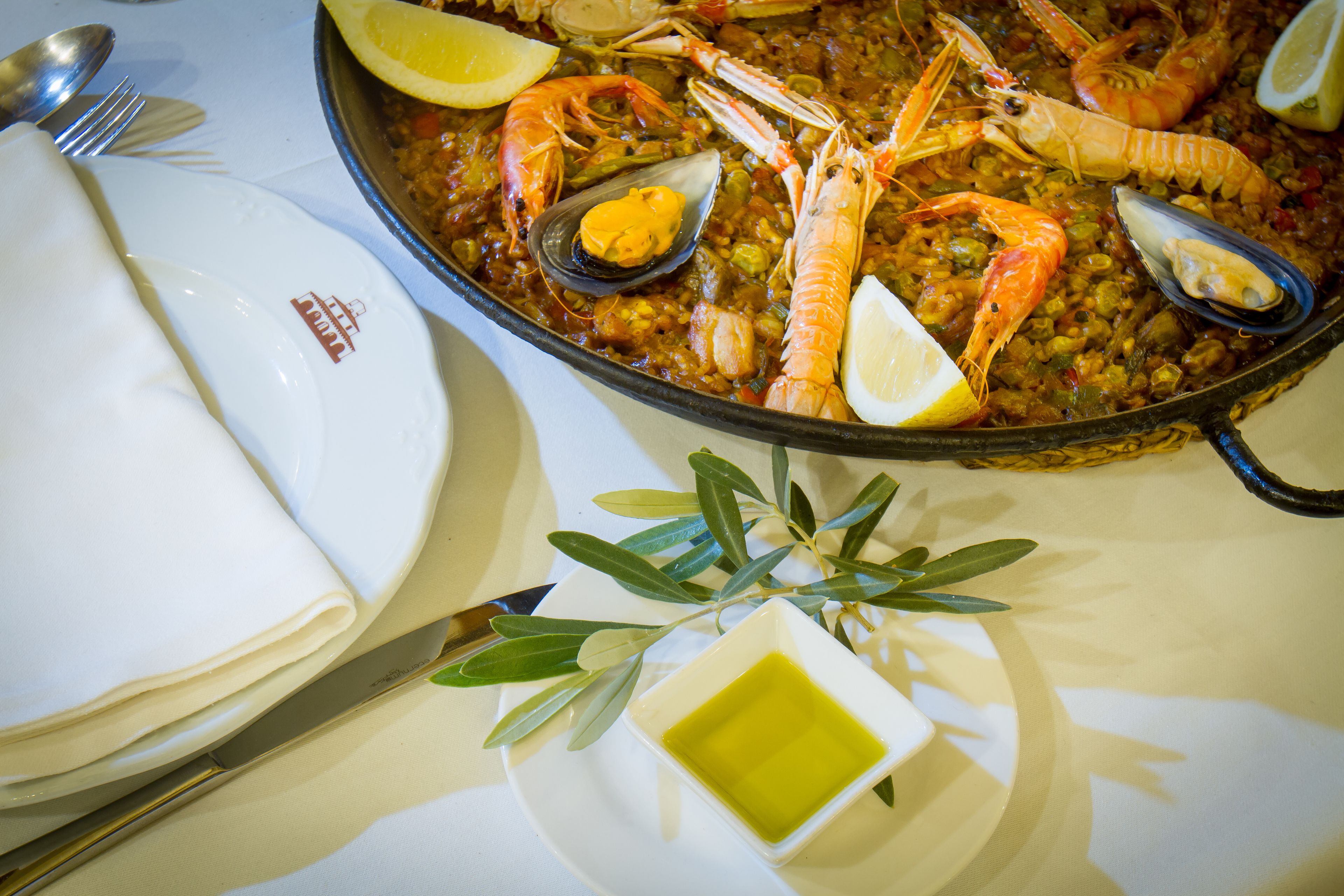 Une paella aux fruits de mer, avec des crevettes, des moules et des tranches de citron, servie sur une table.
