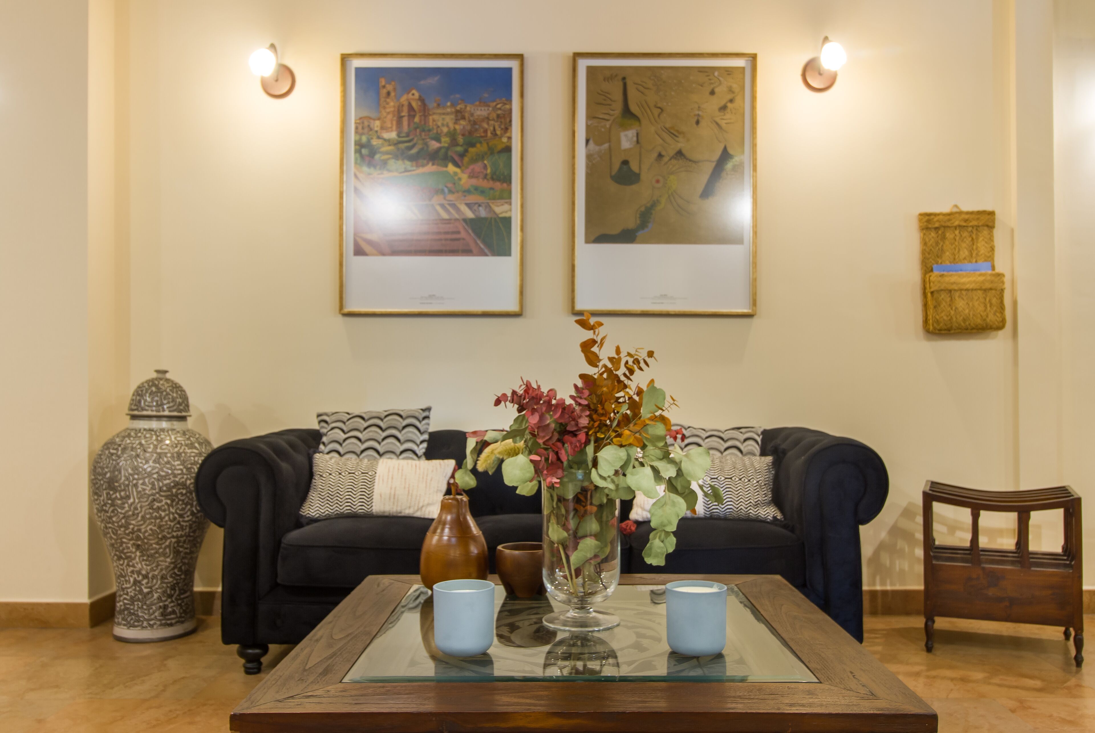 A living room with a sofa, a coffee table, a vase with flowers, and two framed pictures on the wall.