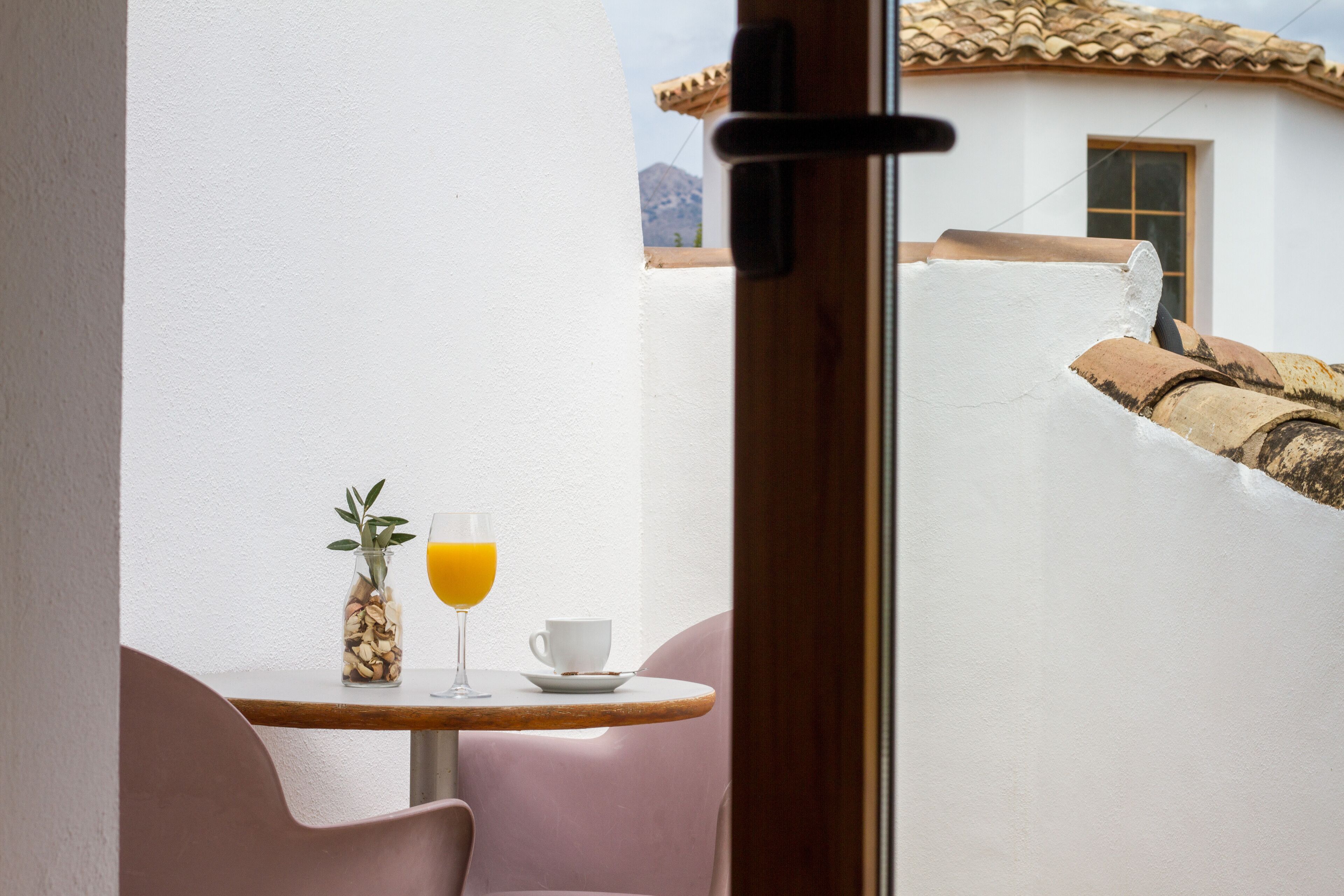 A balcony with a table, a chair, a glass of orange juice, and a cup.