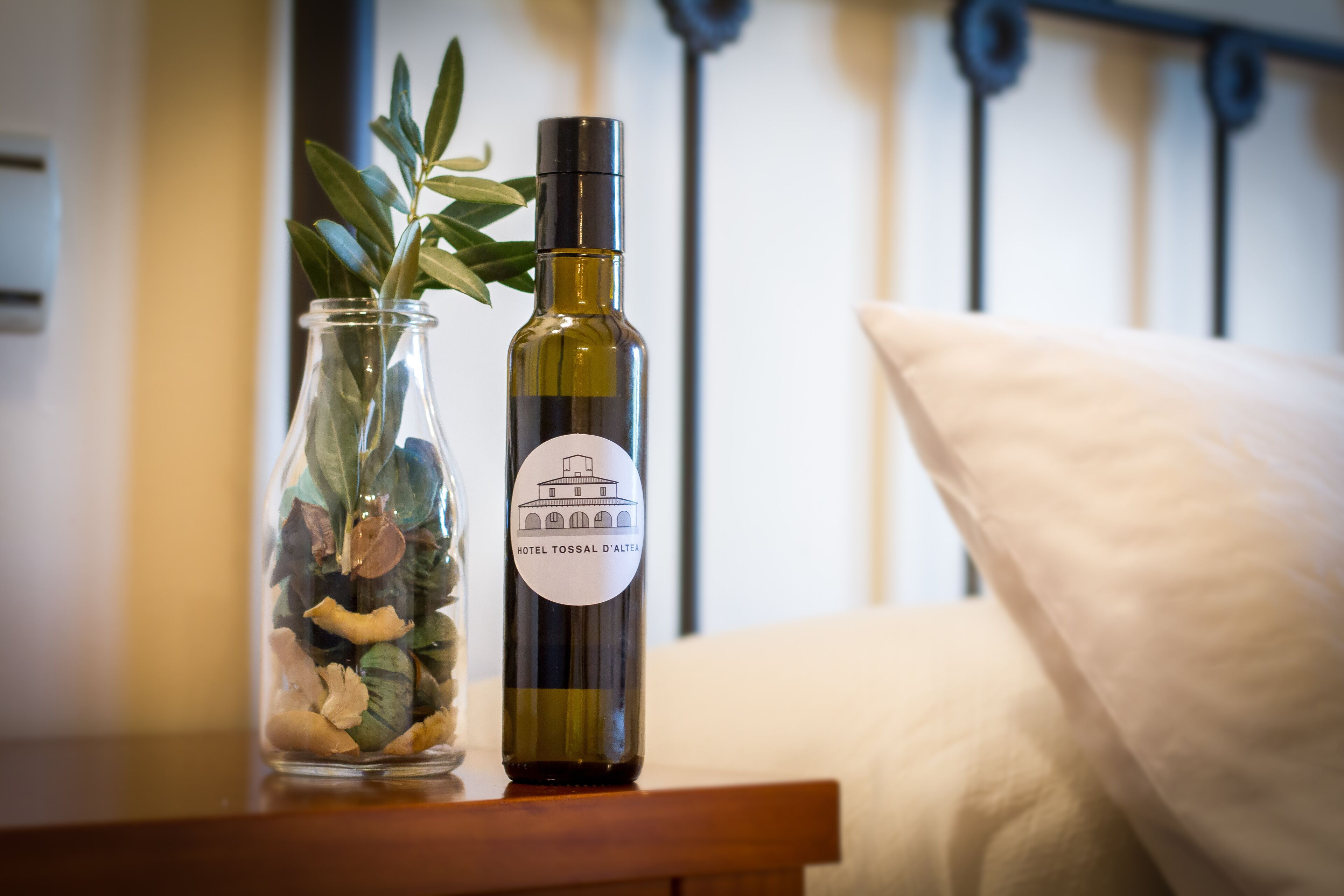 Una botella de vino del Hotel Tossal D'Alaea, una jarra de cristal con piedras decorativas y una planta sobre una mesa de madera.