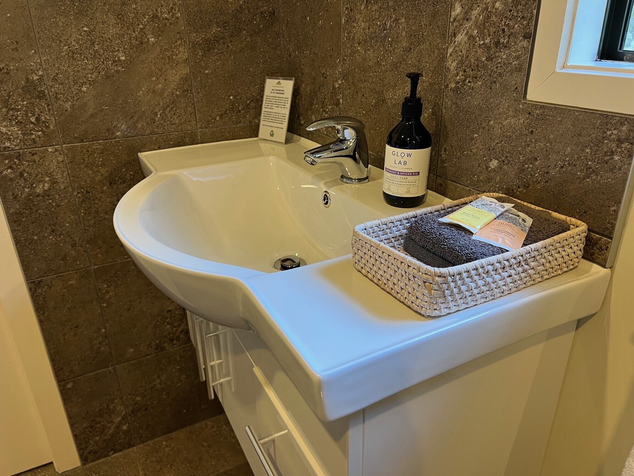 A bathroom sink with a bottle of hand wash soap and a basket of toiletries.