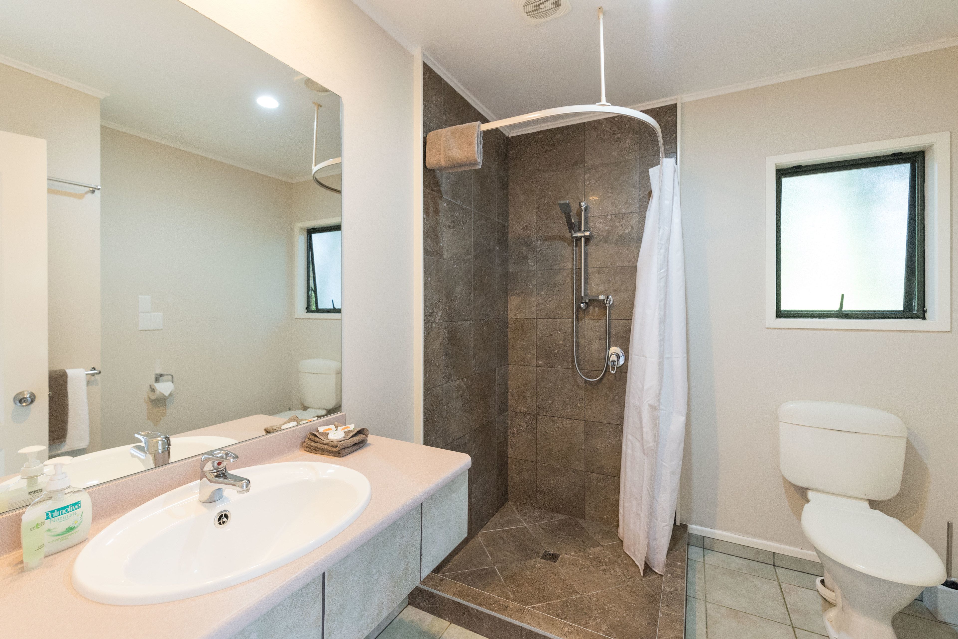 A modern bathroom with a large sink, a shower with a glass door, a toilet, and a window.