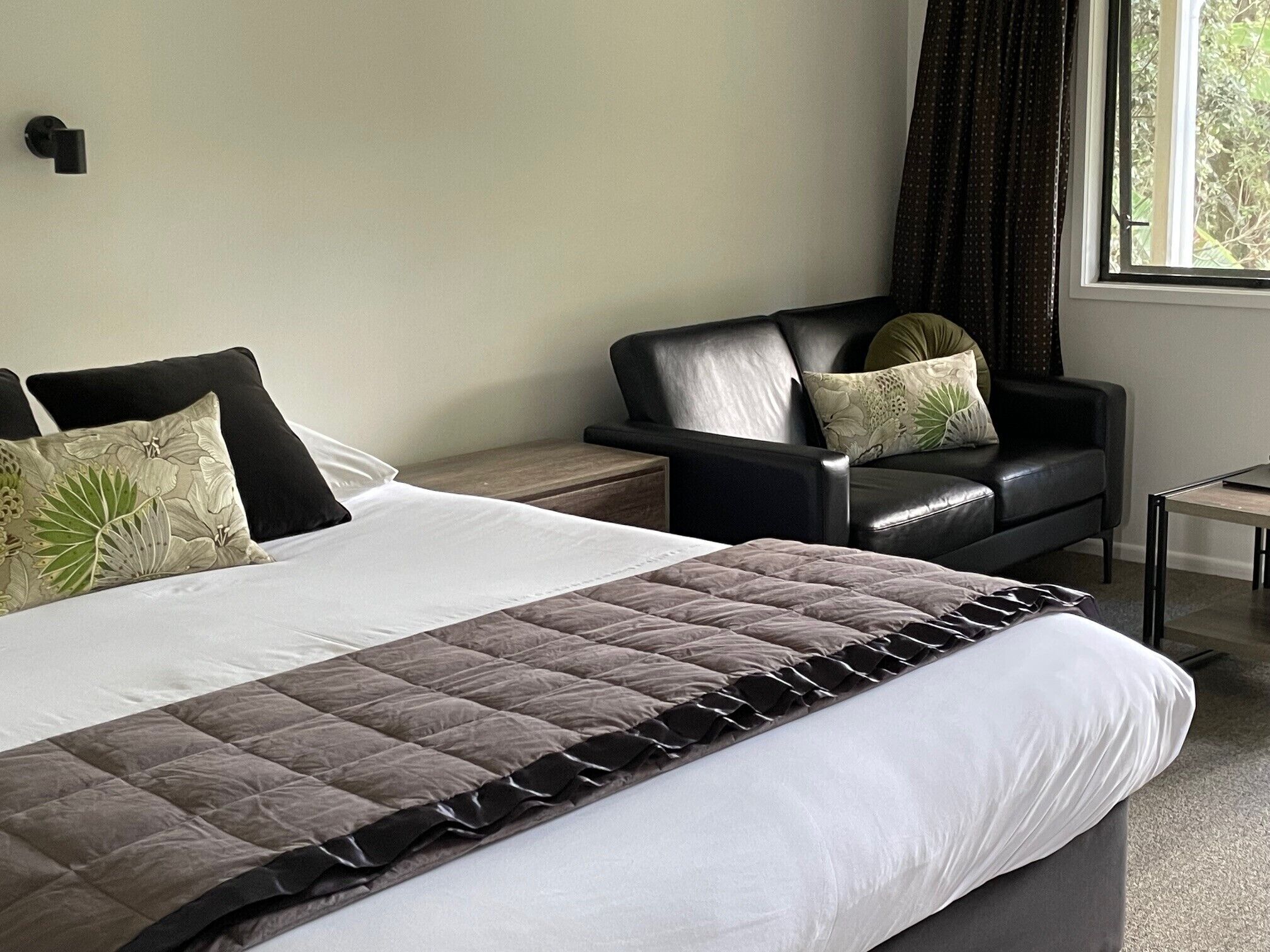 A hotel room with a large bed, a leather sofa, a small table, and a window with curtains.
