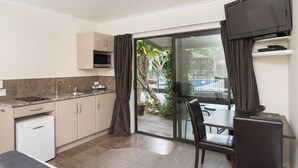 A compact kitchen with a microwave, sink, and a dining area with a table and chairs. - Kauri Park Motel (Kerikeri)