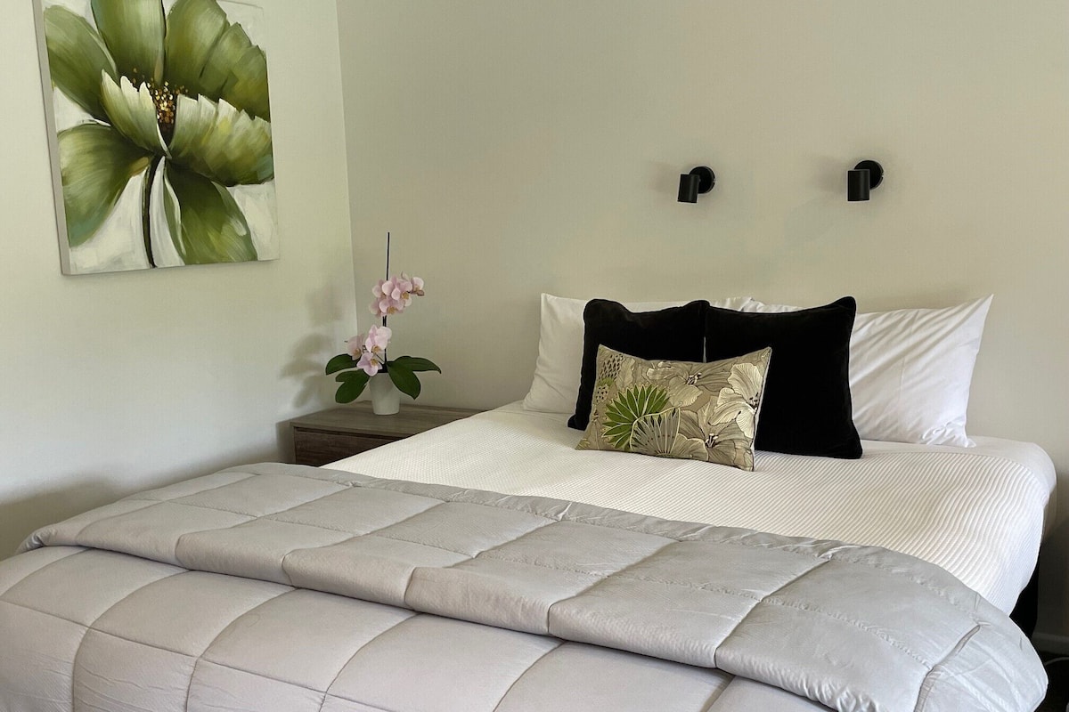 A neatly made bed with a quilted cover, a single decorative pillow, and a wall-mounted nightstand with a vase of flowers.