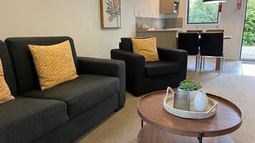 A modern living room with two black sofas, each with a yellow patterned pillow, and a round wooden coffee table with a woven tray and a small plant.